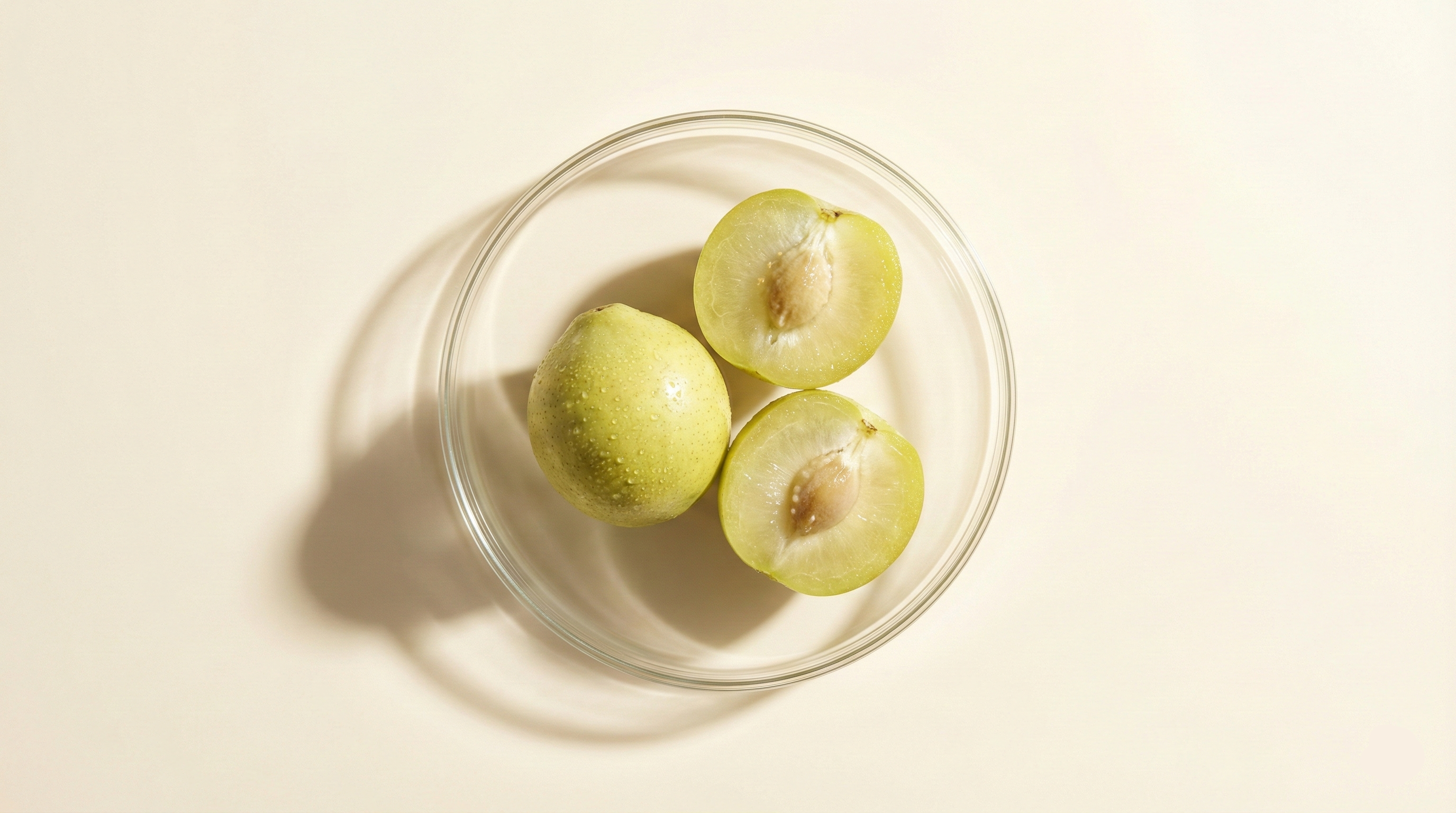 three Kakadu Plums inside a clear glass bowl, set against a plain light beige background